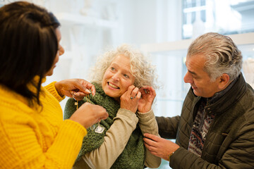 Sales assistant helping senior woman trying on jewelry in shop