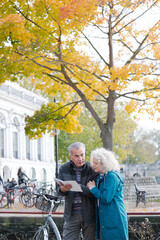 Senior couple with bicycles traveling, looking at guidebook along autumn river