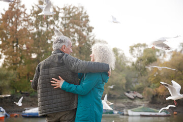 Affectionate active senior couple hugging at park pond