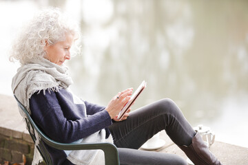 Active senior woman using digital tablet at park pond