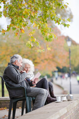 Active senior couple talking, enjoying coffee at autumn park cafe