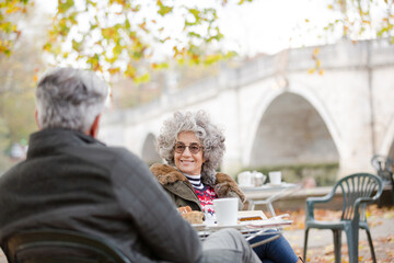 Obraz premium Active senior couple talking, enjoying coffee at autumn park cafe