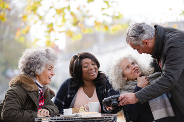 Active senior friends using digital camera at autumn sidewalk cafe