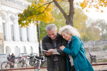 Senior couple with bicycles traveling, looking at guidebook along autumn river