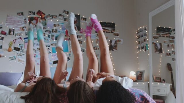 happy teen girls lying on bed at home with legs up having fun wiggling feet hanging out wearing pajamas enjoying relaxing morning on weekend