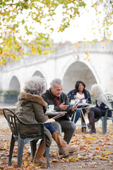 Senior couple using digital tablet, enjoying coffee and tea at autumn park