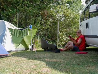 A traveler in a red shirt, with sunglasses and shaved hair, plays the Spanish guitar sitting on the...