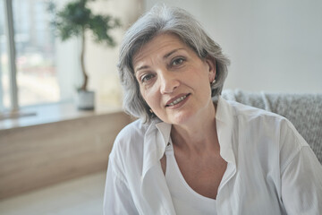 Portrait of a happy senior elderly woman in a bright comfortable apartment. Close up smiling beautiful retired grandmother in living room.