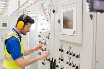 Male worker wearing ear protectors, operating machinery at control panel in factory