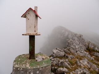 A white wooden birdhouse with a red roof on top of the mountain on a foggy day