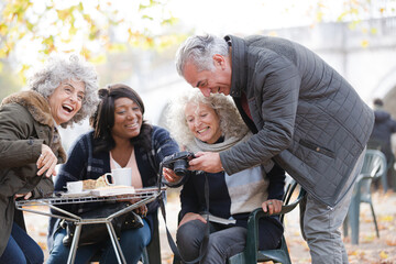 Active senior friends using digital camera at autumn sidewalk cafe