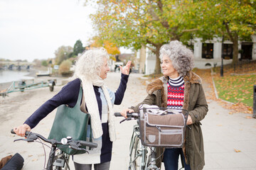 Smiling active senior women walking bicycles in autumn park