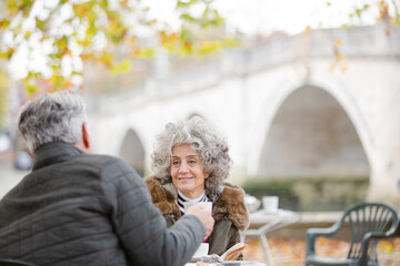 Active senior couple talking, enjoying coffee at autumn park cafe