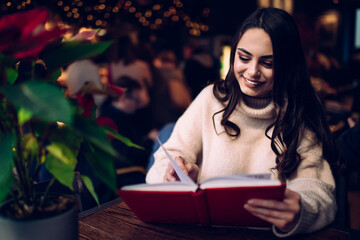 Cheerful young female reading book in cafe