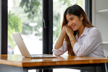 Obraz premium Young asian woman having conference video call using laptop talking to coworker online audience sitting at office desk in evening. 