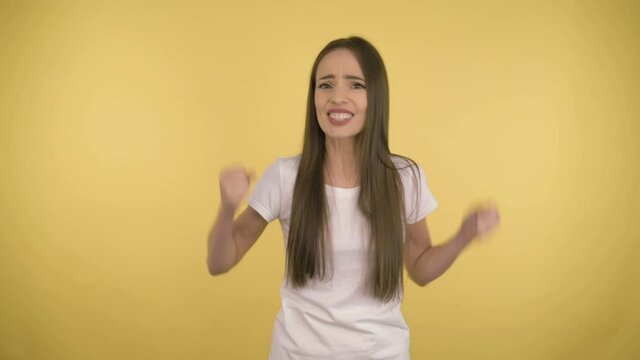Aggresive disappointed woman in doubt. An attractive woman of 35 years old negotias over the current situation. Woman in white t-shirt on yellow background isolated. Studio.