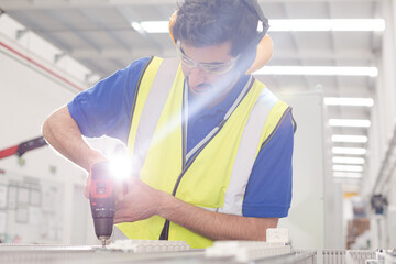 Male engineer with power drill assembling equipment in steel factory