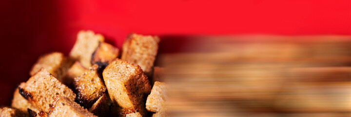 Croutons from black bread on red background. Delicious Fried crunchy crackers. Shallow depth of field image. Food panoramic banner.