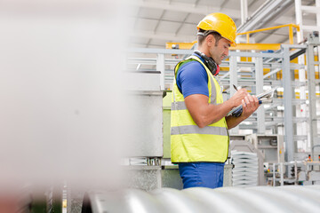 Factory worker with clipboard inspecting steel parts in factory