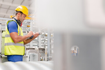 Factory worker with clipboard inspecting steel parts in factory