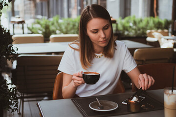 Young smiling woman drinks coffee in a street cafe