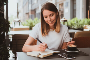 Stylish business woman in a street cafe making notes in a notebook and drinks coffee