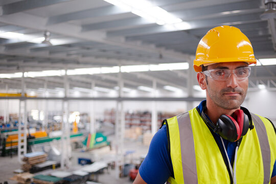 Portrait serious male worker in protective eyewear and hard-hat in factory