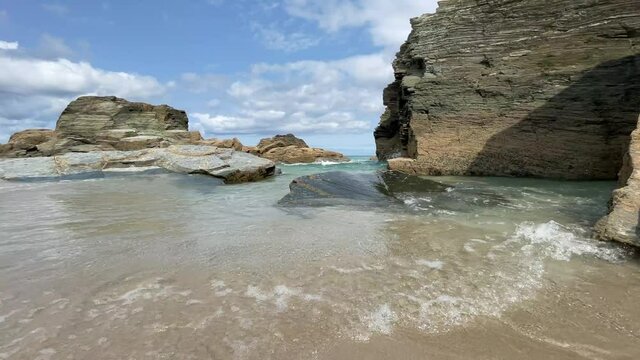 Beach with large rocks where the sea water approaches the shore in a calm and delicate way. Beautiful sky with white clouds. High quality 4k footage