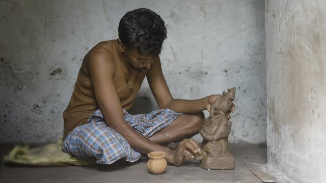 Medium shot of Concentrated artist making clay ganesh idol for ganesh or vinayaka festival at home - concpet of hindu religious festival preparations in India.
