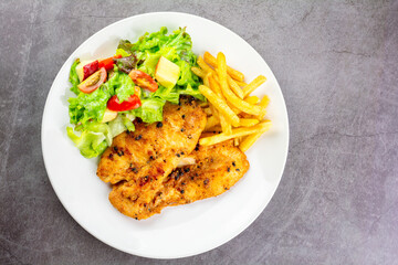 Homemade food concept. Chicken breast steak with black pepper served with salad and french fries in a white dish. Hight protein food. Top view.