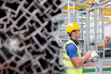 Factory worker with clipboard inspecting steel parts in factory