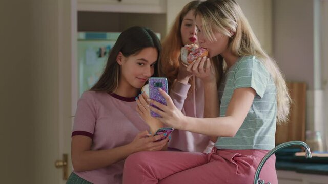 funny teenage girls posing with donuts taking photos using smartphone sharing on social media enjoying hanging out on weekend in kitchen