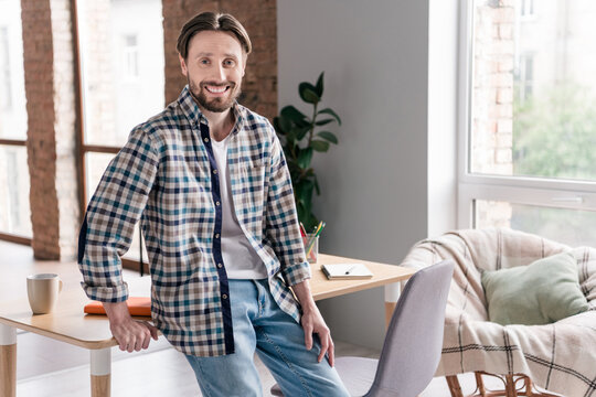 Photo of pretty adorable young man wear plaid shirt sitting table smiling indoors house office