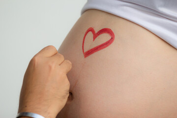 Closeup image of beautiful pregnant woman belly with heart painted. Husband paints a heart on his wife's belly.