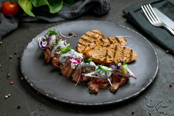 Sliced roast beef with mushrooms and onion on sour cream on dark stone table