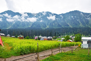 Scenic view of village with high green mountains behind under cloudy sky