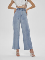 Naklejka premium Young elegant woman with long straight hair and natural make-up in white blouse and blue jeans standing and posing on bright grey background