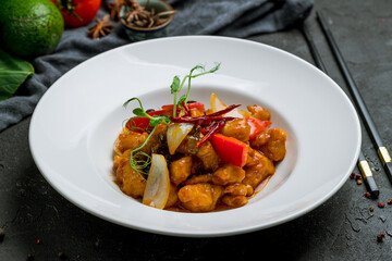 Sichuan fried chicken in sauce on white plate on dark stone table