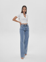 Young elegant woman with long straight hair and natural make-up in white blouse and blue jeans...