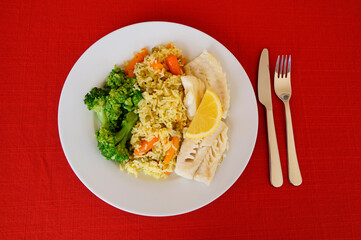 a platter with delicious fried codfish dish with rice and various vegetables and a slice of juicy lemon