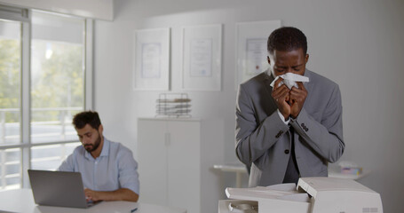 Sick afro manager blowing nose in paper napkin working in office