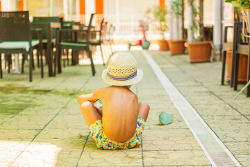 a child with a hat sitting by the pool on a sunny summer day.  little boy with a summer hat type chapel. 
