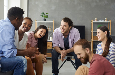 Young mixed race people having fun and enjoying good time together. Diverse group of six happy millennial friends sitting on the sofa in the living-room and laughing at a funny joke - obrazy, fototapety, plakaty