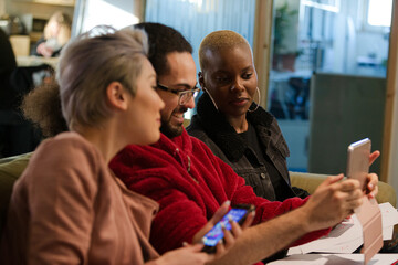 Three colleagues sitting on sofa, discussing paperwork, laughing