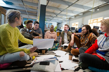 Team sitting on office floor, discussing paperwork