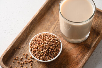 Healthy buckwheat milk in glass with grain ingredient in wooden tray on a white background. Horizontal orientation. Close up.