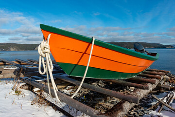 A bright, colorful, orange and green wooden sailing vessel, wood boat, on the shoreline of a bay....