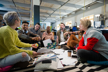 Team sitting on office floor, discussing paperwork