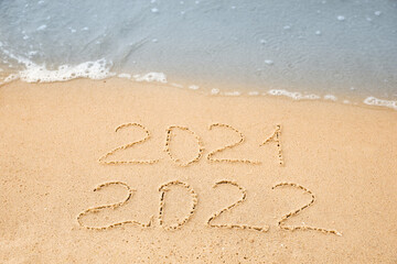 Dates written on sandy beach. 2021 washed by sea wave as New 2022 Year coming