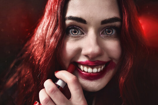 Halloween Time. Portrait of crazy-looking psycho woman with red hair she is smearing red lipstick on her face. horror,Fear and nightmare concept